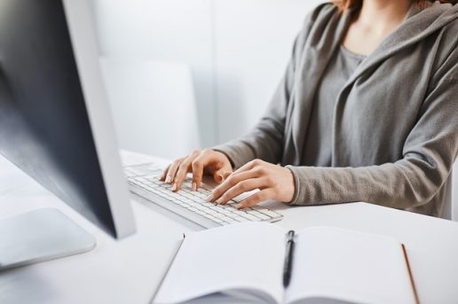 Working hard to party hard on weekends. Cropped shot of woman typing on keyboard, sitting in front of computer monitor. Freelancer translating new project, writing some notes in note pad. Office and work concept